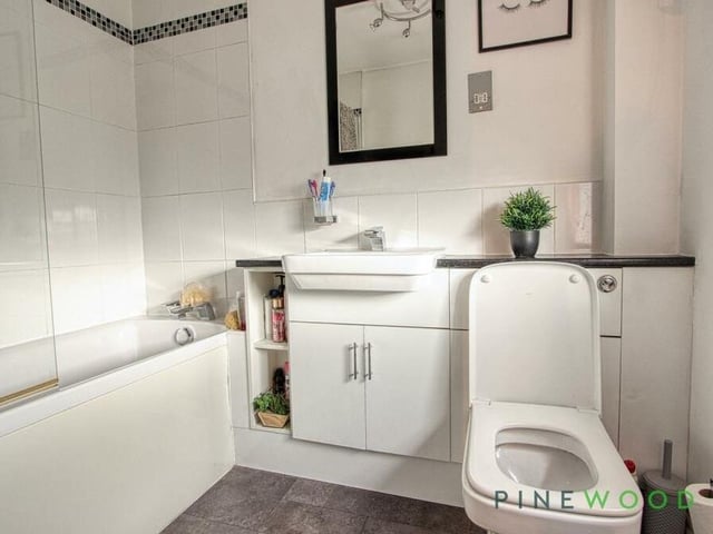 Here is the en suite bathroom to the master bedroom. It features a bath tub with a mains shower, vanity-style sink unit, low-flush WC, towel radiator and vinyl flooring.
