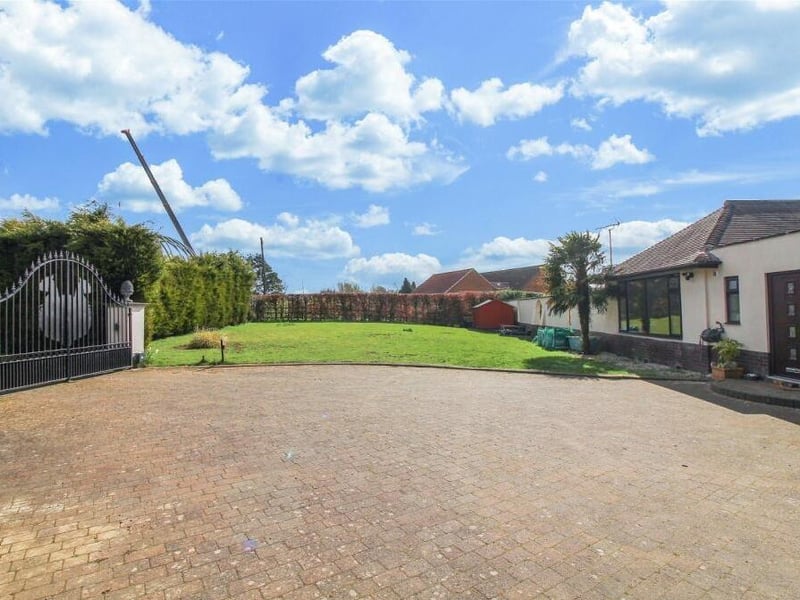 A ground-level shot of the private and enclosed front garden, showing gates, drive, lawn, hedgerow borders and front door.