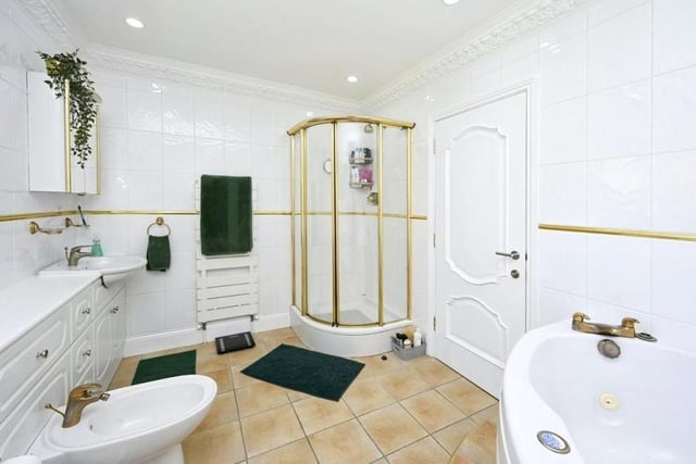 A sparkling bathroom that is fitted with a white suite comprising corner spa bath, separate shower cubicle, low-level WC with bidet, two wash hand basins with vanity storage under, heated towel-rails and tiled walls and floor.