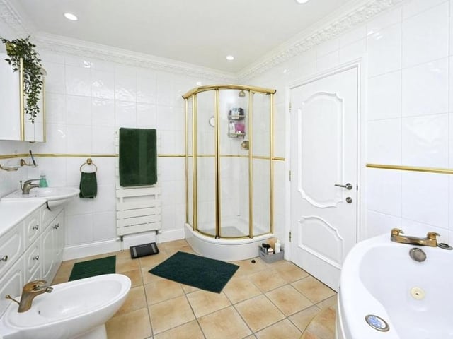 A sparkling bathroom that is fitted with a white suite comprising corner spa bath, separate shower cubicle, low-level WC with bidet, two wash hand basins with vanity storage under, heated towel-rails and tiled walls and floor.