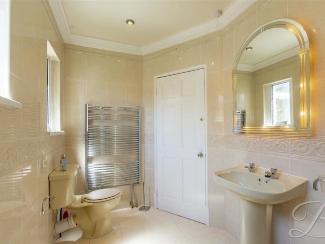 A second look at the family bathroom on the first floor. Spot a low-flush WC, heated towel-rail, pedestal hand wash basin, tiled flooring, downlighting and ceramic tiled walls.