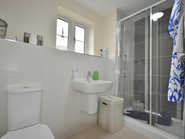 Here is the modern en suite shower room to one of the bedrooms on the first floor. It boasts a fully tiled, double-width shower enclosure with wall-mounted chrome shower,  wall-hung wash hand basin with chrome mixer tap, and low-flush WC. There is also a chrome, heated towel-rail, tiled display shelf and vinyl floor.