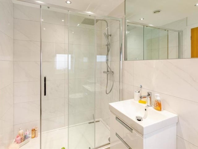 The sparkling en suite facilities attached to the second bedroom include a walk-in, tiled shower enclosure with 'rainfall' shower and additional handset. There is also a vanity unit with inset wash hand basin and two storage drawers beneath, plus a low-flush WC, chrome, heated towel-rail, modern tiling, vinyl floor and five ceiling spotlights.