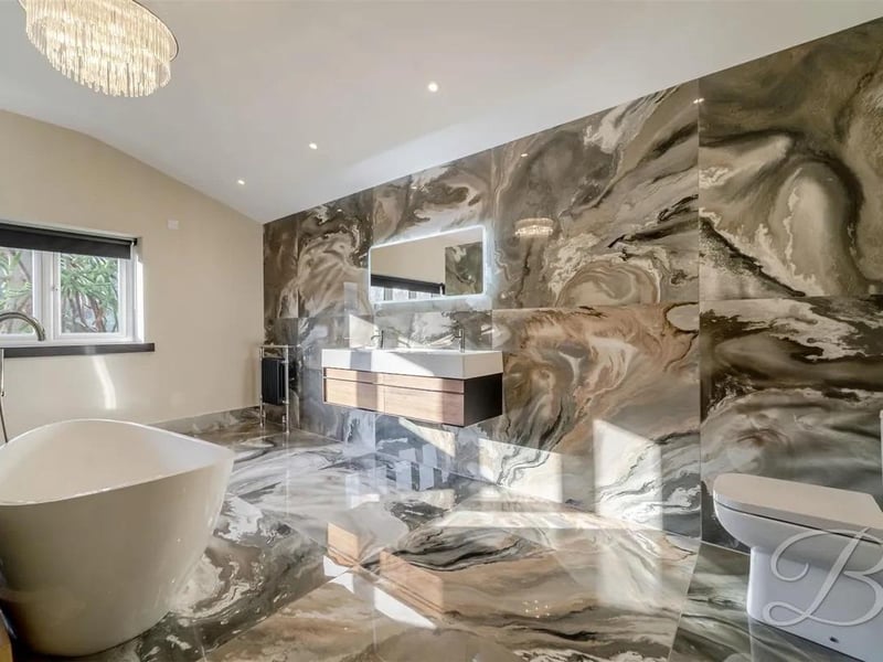 An exceptional, fully tiled four-piece en suite bathroom featuring a double hand wash vanity, a low-flush WC, and a freestanding bath, combining modern elegance with practical luxury.