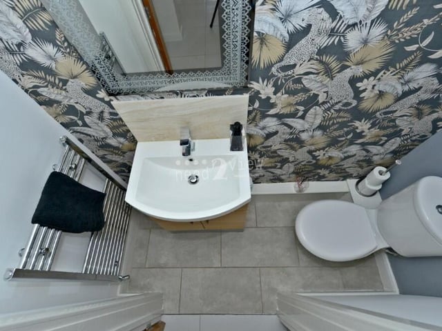 Completing our look at the ground floor is this toilet, which comprises a WC, wash hand basin, built into a vanity unit, chrome towel-radiator and ceiling light point.