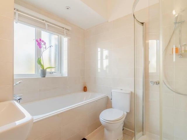 The family bathroom at the £690,000 property comprises a modern, white suite with chrome fittings. There is a tiled inset bath-tub with mounted mixer tap and shower handset, plus a separate, tiled shower cubicle, vanity unit with inset wash hand basin and storage drawer beneath, and low-flush WC. A chrome, heated towel-rail, tile-effect laminate floor and five ceiling spotlights complete the look.