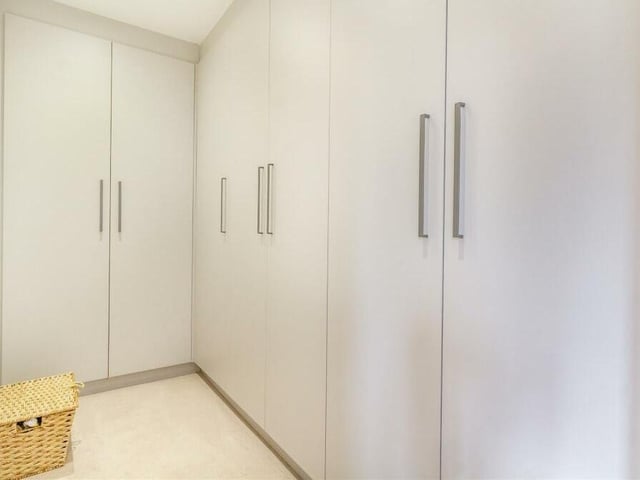 A walk-in wardrobe area, attached to the master bedroom, features extensive and modern fitted wardrobes with hanging rails and shelves.