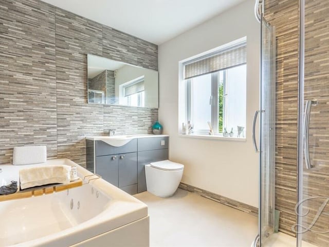 The attractive family bathroom includes a panelled Jacuzzi bath, shower enclosure, low-flush WC, wash hand basin with vanity storage and modern tiling.