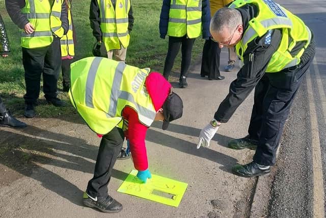A 'mini police officer' sprays the pavement, under the guidance of a Derbyshire Police officer. Mini Police from the Model Village Primary School have been learning about road safety and how to keep themselves and other road users safe.