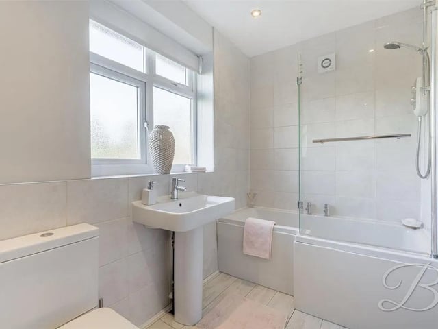 A modern suite finished in white comprising P shaped bath with shower over, low level WC and pedestal wash basin with complementary tiled splashbacks. Opaque window and heated towel rail.