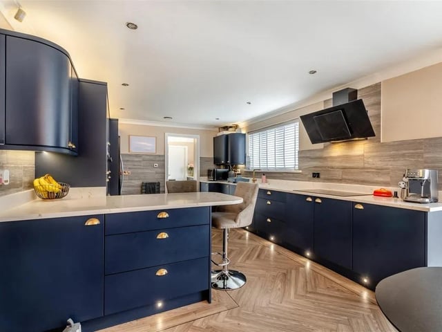 Having contemporary navy blue shaker cabinets comprising wall cupboards with under lighting, base units and drawers complemented by Calacatta quartz worktops. Inset 1 1/2 bowl Villeroy & Boch ceramic sink with brass mixer tap. Two integrated Bosch ovens, an oversized four ring induction hob with contemporary extractor hood above. Peninsula island with space for stools underneath. Space for an American style fridge/freezer.
