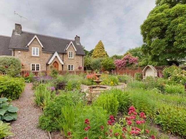Let's step outside now for another look at the front of The Hollies. A timber gate opens on to a garden with gravelled paths running among a variety of mature shrubs and flowers, and a central water feature.