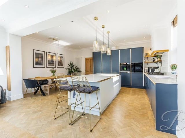 This impressive open-plan kitchen, living, and dining area is designed with a stylish array of wall and base cabinets, integrated appliances, and elegant splashback tiles. A standout feature of the space is the central island, offering extra storage and a convenient breakfast bar.