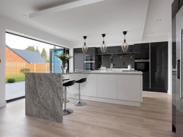 The stunning open-plan family living kitchen boasts a range of contemporary high gloss contrasting cabinets complemented by quartz worktops. There is an L-shaped island with inset sink.