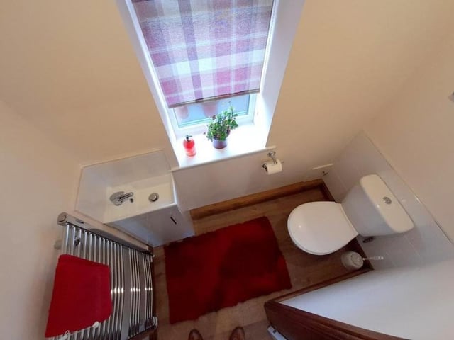 An overhead shot of the downstairs cloakroom. It comprises a low-flush WC, wash hand basin with cupboard underneath, chrome heated towel-rail, laminate floor, coving and recessed spotlights to the ceiling.