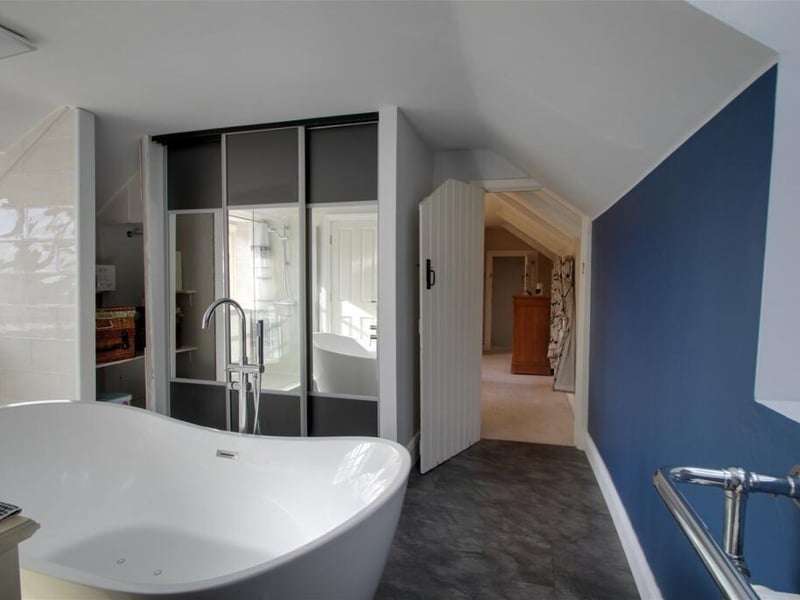 Attached to the principal bedroom is this en suite bathroom. It features a free-standing spa bath, a double walk-in shower, low-flush WC, wash basin with vanity unit beneath, and double wardrobes with sliding doors, providing useful storage.