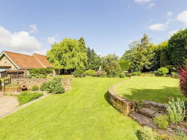 The stunning, wrap-around landscaped garden offers something truly special. At its centre is a generous green lawn, bordered by mature trees, tall hedging, and beautifully arranged flower beds.