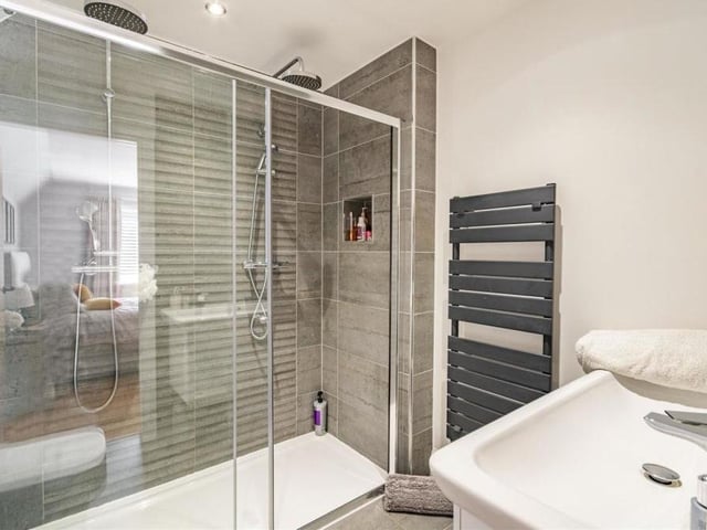 This is the smart and superbly appointed en suite to the master bedroom.  There is a large, tiled shower enclosure, with his and hers 'rain' showers, a wall-hung sink with matching mixer taps and storage drawers beneath, and a low-flush WC. It also includes chrome fittings and a heated towel-rail.