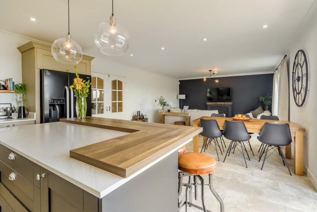 Here is the first shot of the open-plan living, dining and kitchen area, which sits at the heart of the home. It is superbly appointed, with a central island that has feature lighting above and contemporary shaker cabinets, including base units and drawers, marble-effect work surfaces and a raised butcher's block-style work surface