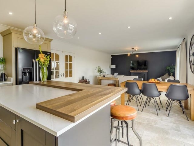 Here is the first shot of the open-plan living, dining and kitchen area, which sits at the heart of the home. It is superbly appointed, with a central island that has feature lighting above and contemporary shaker cabinets, including base units and drawers, marble-effect work surfaces and a raised butcher's block-style work surface