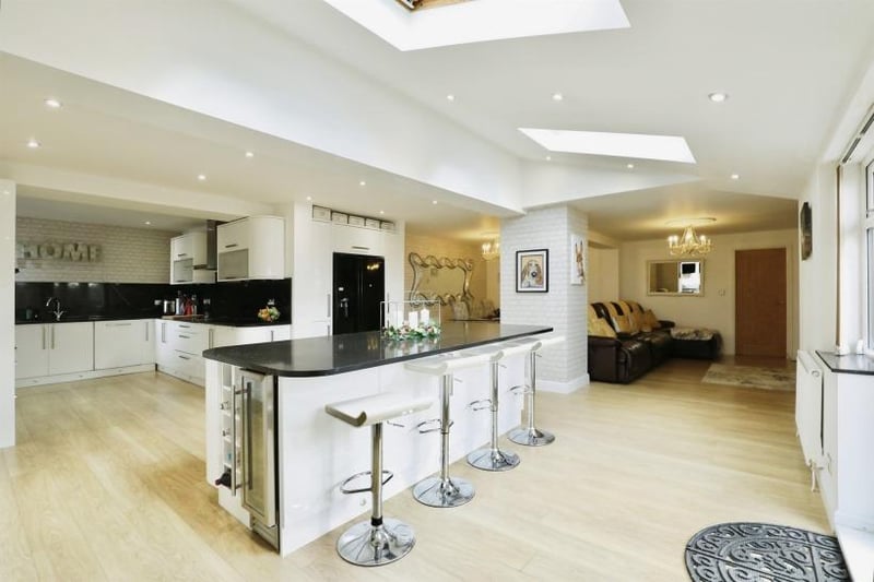 The first room to look at is the modern, fitted high-gloss kitchen in one of the properties. It features a range of units, black granite work surfaces, breakfast bar with granite top, an integrated double oven, microwave and steam oven, plus an induction hob with hood and extractor over. A pillar separates a dining and living area.