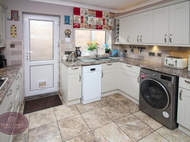 Our third shot of the kitchen shows how there is space and plumbing for essentials such as a washing machine and dishwasher. Tiled flooring and a chrome, heated towel-rail add to the room's appeal. The door leads to the side of the bungalow.