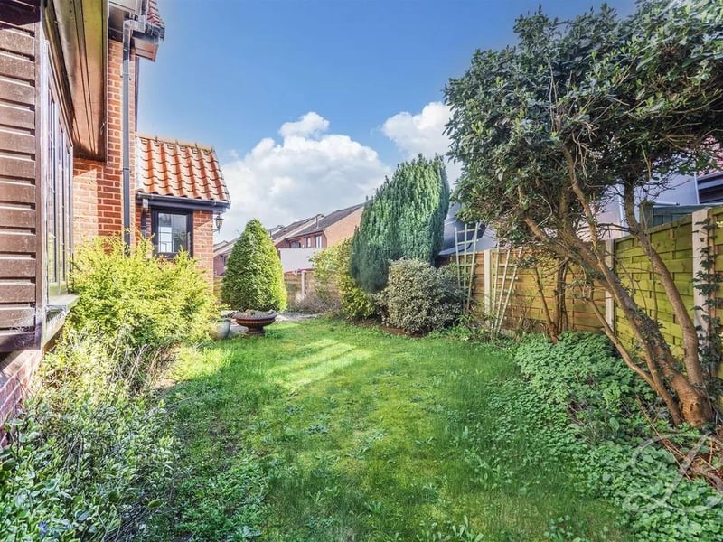The rear garden features a well-maintained lawn, a paved patio area, and a wooden pergola, creating an inviting space for outdoor relaxation and entertaining.