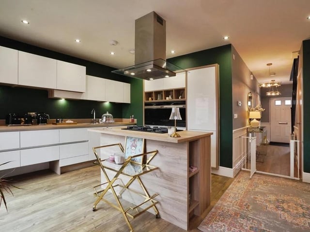 The kitchen is equipped with modern appliances, including a central island housing a gas hob and extractor above. Wood-effect work surfaces complement the warm wood flooring that runs throughout. Large patio doors open directly to the rear garden, flooding the space with natural light and providing easy access to outdoor dining and entertaining