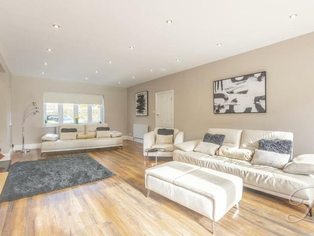 A second shot of the lounge or living room, which is full of natural light, with a window to the front of the house and downlights. The floor is laminated.