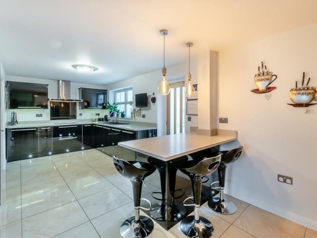 And so on to the contemporary kitchen/breakfast room, which boasts a range of high-gloss, black cabinets with large, brushed stainless steel handles. In the foreground, you can see an island breakfast bar with two drawer units below, dropped lights above and space for stools