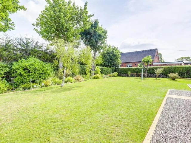 The garden features a well-maintained lawn, a vegetable patch, gravelled borders, various shrubs and trees — including apple, plum, and pear trees — all enclosed by mature hedge boundaries.