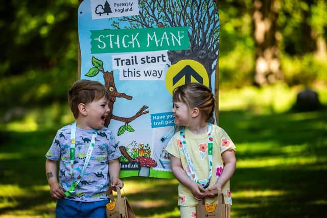 Two young children standing in front of a Stick Man activity trail panel.