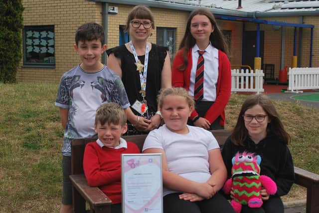 Mental health lead Melissa Winterton with pupils, the award and a worry monster on the school's friendship bench.