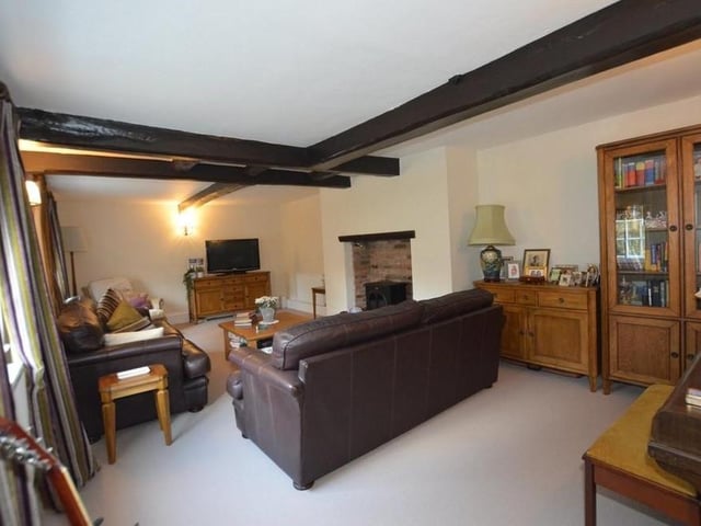 A second look at the living room, which is 26 feet long. It includes a feature fireplace with a stone hearth and brick inset, three radiators and wall lights.