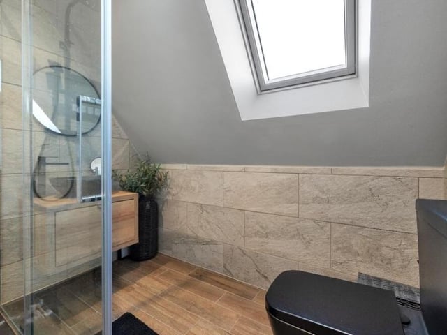 A second glance at the shower room, which has fully tiled walls and flooring, a black low-flush WC, towel radiator, LED spotlights to the ceiling and a double-glazed Velux window.