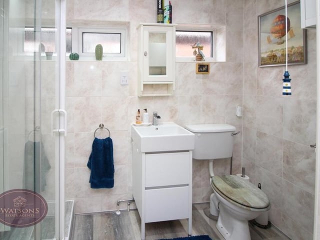 The bungalow's shower room is a three-piece suite in white that comprises a shower cubicle, WC and vanity unit with wash hand basin and storage drawers. The floor is laminated and the walls are tiled.