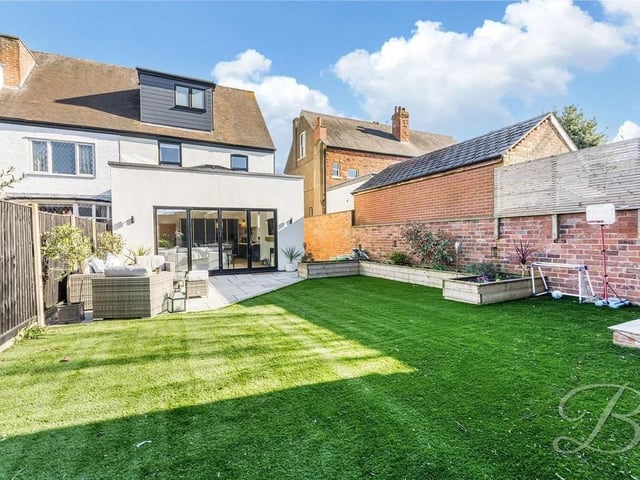 The rear garden is a real highlight, with an artificial lawn, a patio seating area, decorative shrubs, and a fenced perimeter providing a sense of privacy.