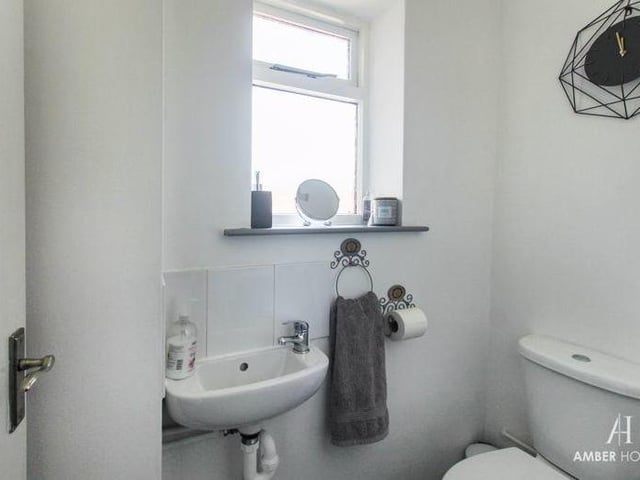Close to the entrance hall is this downstairs toilet, featuring a low-level WC and wall-mounted hand basin. There is also vinyl flooring, splashback tiling, a radiator and a double-glazed window to the side of the house.