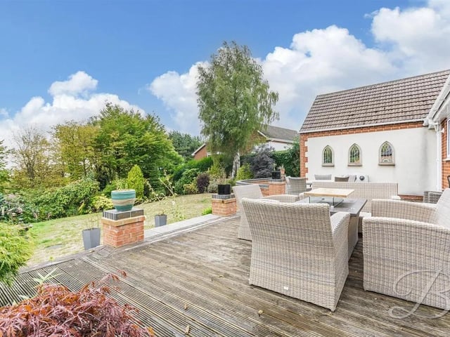 The rear garden is a standout feature, with a decked seating area leading down to a vast lawn, surrounded by mature trees and shrubbery, offering a private and tranquil outdoor space for relaxing, entertaining, or enjoying family life.