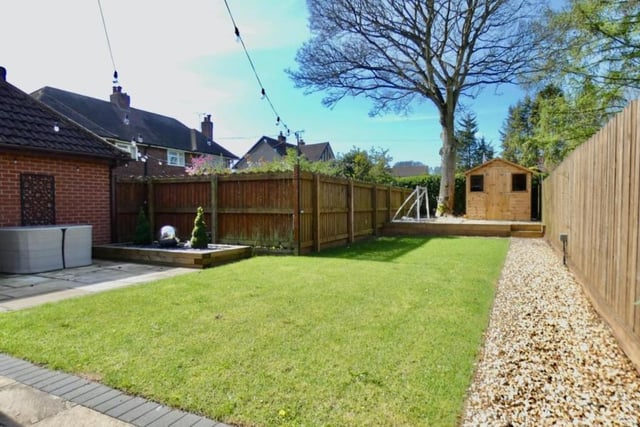 The sunny back garden features a manicured lawn and a raised gravelled area with a summer house.