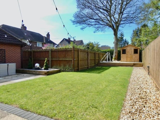 The sunny back garden features a manicured lawn and a raised gravelled area with a summer house.