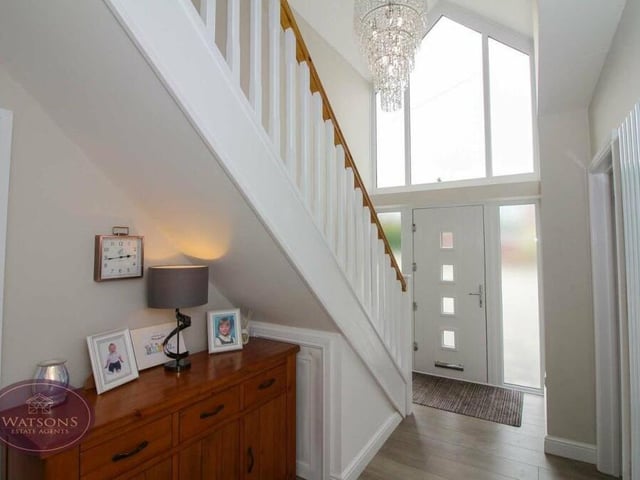 As we prepare to go upstairs to the first floor, let's pass through the entrance hall. It has a feature window above the front door, chandelier light, vertical radiator and a storage cupboard, as well as under-stairs storage.