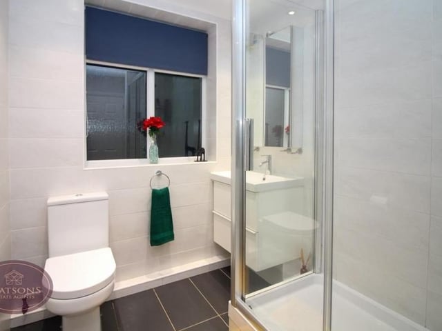 This shower room is made up of a white three-piece suite that comprises a shower cubicle, wall-mounted sink and WC. There are also ceiling spotlights and an obscured window to the side of the property.