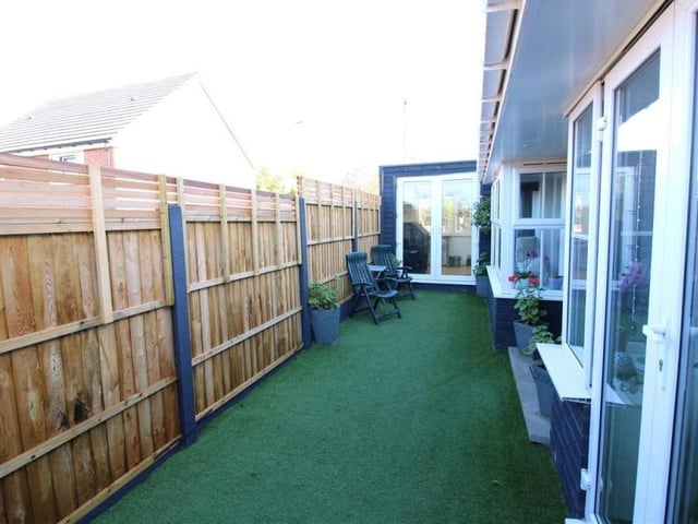 This is the first of a handful of photos showing the exterior of the two-bedroom bungalow. It features the front of the property with a seating area that has artificial grass and fenced borders.