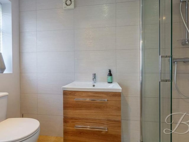 Here is the en suite shower room to the master bedroom on the first floor. It consists of an enclosed shower, low-flush WC, wash hand basin with vanity storage, and full-height tiling.