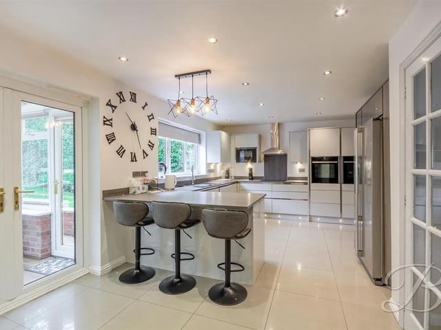 The contemporary kitchen features tiled flooring, sleek high gloss units, extended worktops ideal for additional seating, and a range of integrated appliances.