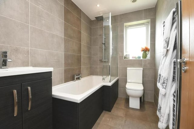 Before we take a look at the other two bedrooms, here is the modern family bathroom. It consists of a P-shaped bath with mixer tap and rainfall shower over, a wash hand basin with vanity unit, WC, fully tiled walls and splashbacks, tiled flooring and towel radiator.
