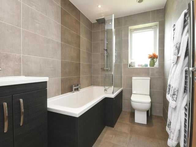 Before we take a look at the other two bedrooms, here is the modern family bathroom. It consists of a P-shaped bath with mixer tap and rainfall shower over, a wash hand basin with vanity unit, WC, fully tiled walls and splashbacks, tiled flooring and towel radiator.