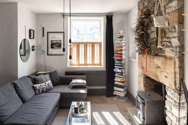 This room has flagstone flooring, exposed stone wall surround a log-burning stoves and shuttered sash windows.