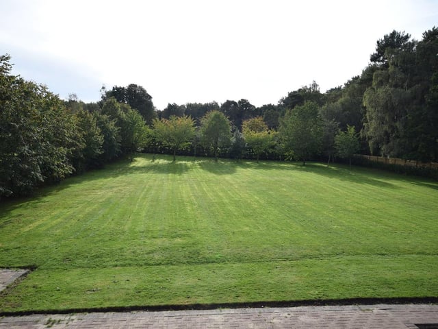 The garden, with its extensive lawn and surrounding trees, spreads out in front of you as you stand on the balcony in the main bedroom.